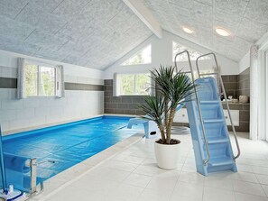 Ein Hallenbad mit Rutsche, einem Kübelpalmenbaum und einer Leiter.