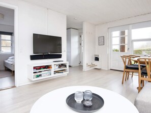A modern living room with a flat-screen TV, a dining area with wooden chairs, and a white entertainment unit with books and a radio. - 6 Person Holiday Home in Borkop (Borkop)