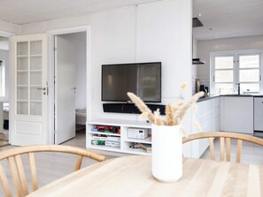 A modern kitchen with white cabinetry, a flat-screen TV mounted above the counter, and a dining area with a wooden table and chairs. - 6 Person Holiday Home in Borkop (Borkop)