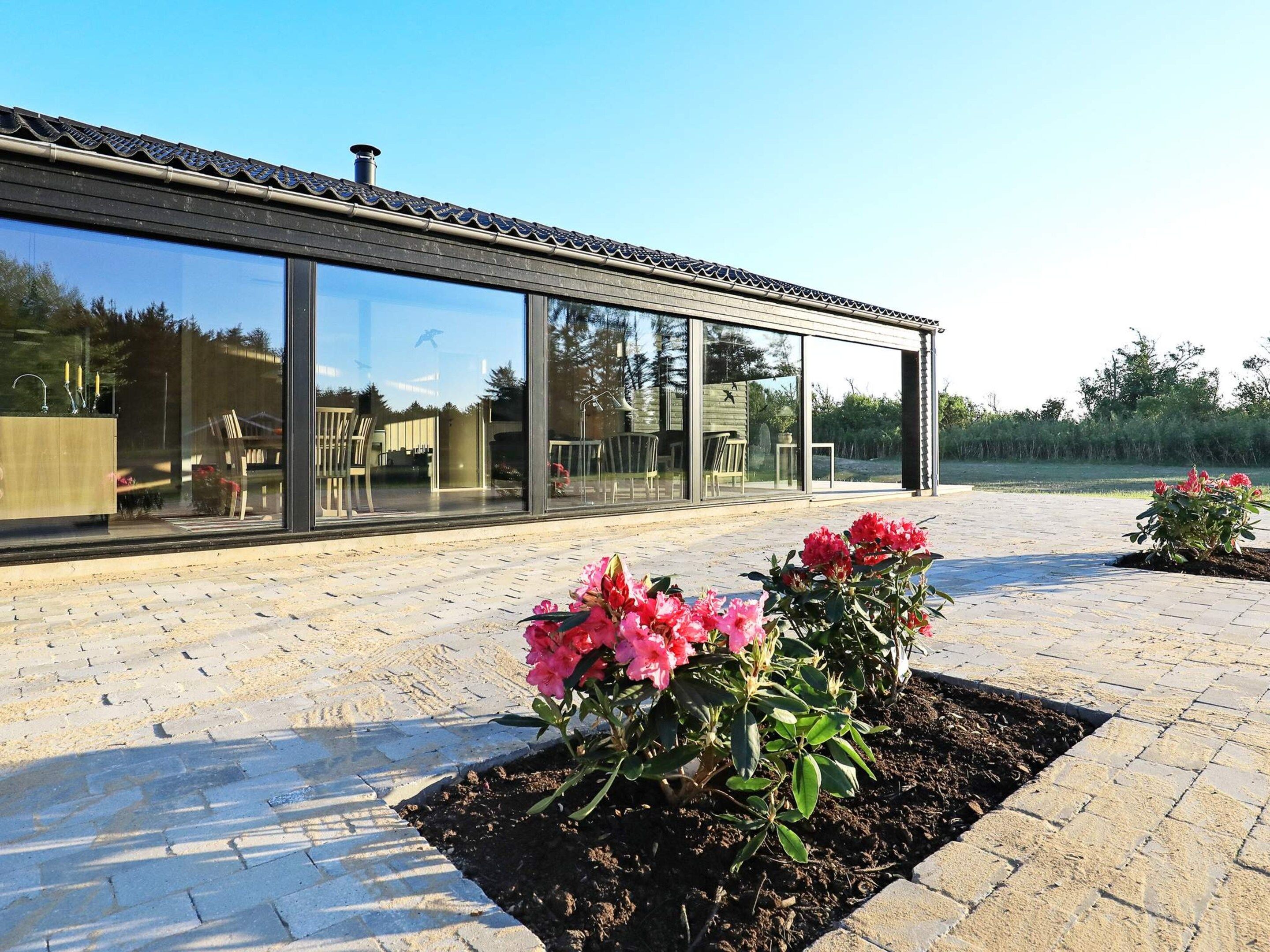 Ein modernes Gebäude mit großen Glasfenstern und einer gepflasterten Außenanlage mit Blumenbeeten.