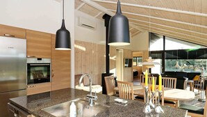 A modern kitchen with a granite countertop, stainless steel appliances, and wooden cabinetry. There is a dining area with a table and chairs, and a view of the outdoors through large windows. - 5 Star Holiday Home in Hjorring (Hjørring)
