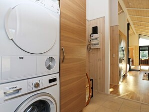 A modern laundry room with stacked washing machines and dryers, wooden paneling, and an open layout leading to a dining area.