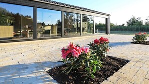 A modern building with large glass windows and a paved area with flowering plants. - 5 Star Holiday Home in Hjorring (Hjørring)