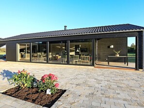A modern building with large glass windows, a flat roof, and a paved area with plants. - 5 Star Holiday Home in Hjorring (Hjørring)
