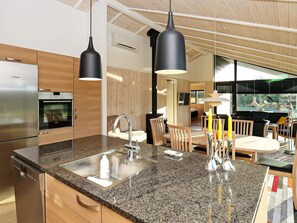 A modern kitchen with a Bosch refrigerator, granite countertop, stainless steel sink, and black pendant lights. - 5 Star Holiday Home in Hjorring (Hjørring)