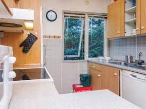 A compact kitchen with a window, a clock, and a dishwasher.