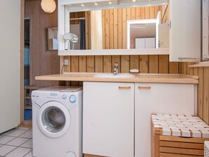 A compact kitchen with a built-in washing machine, wooden cabinets, and a small bench. - Fantastic Holiday Home in Knebel With Wifi (Knebel)