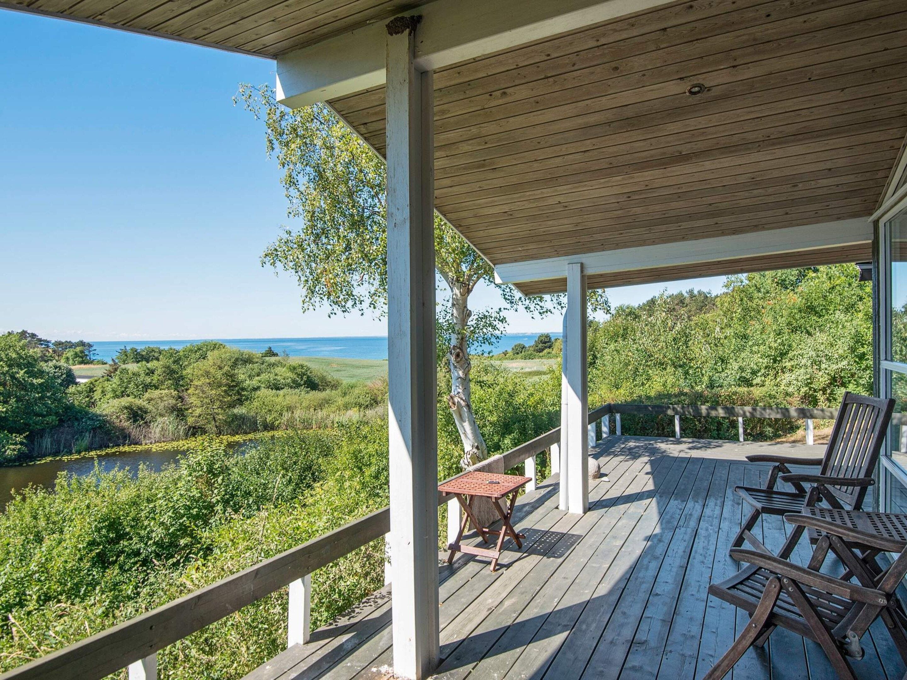 A wooden deck with outdoor furniture, overlooking a natural landscape with trees and a body of water.