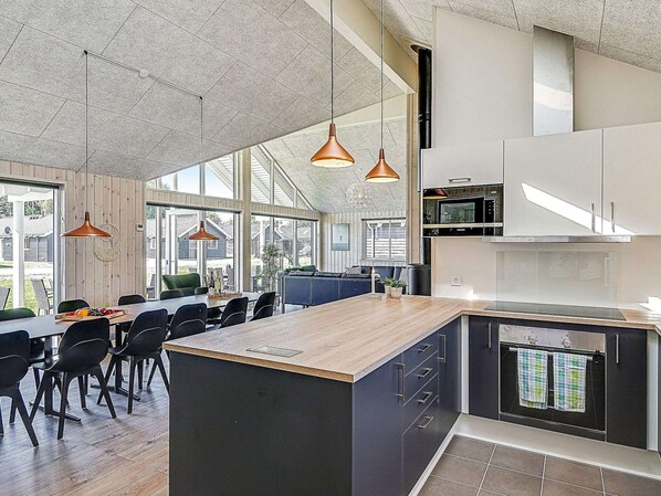 A modern kitchen with a central island, pendant lighting, and large windows.
