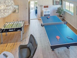 A room with a foosball table, ping pong table, and a foosball table in the background.