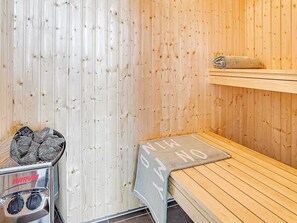 A sauna room with wooden walls, a bench, a towel, and a metal container with stones. - Holiday Home in Kappeln (Kappeln)