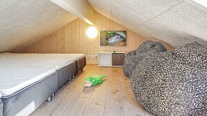 Quarto com teto inclinado, uma cama, um sofá, uma TV e um brinquedo verde pequeno.