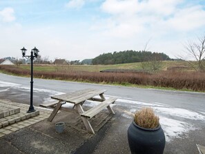 A picnic table with a lamp post nearby, set against a rural backdrop with a road and fields.