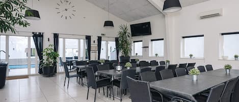 A modern dining area with a large table, chairs, ceiling fans, and potted plants.