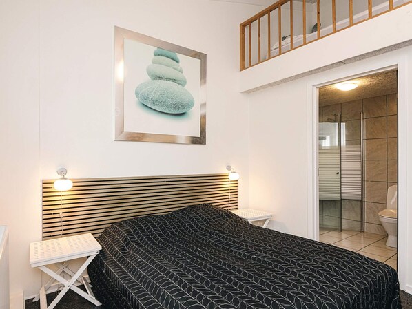 A bedroom with a bed, a bedside table, a framed artwork, and a bathroom with a shower and toilet.