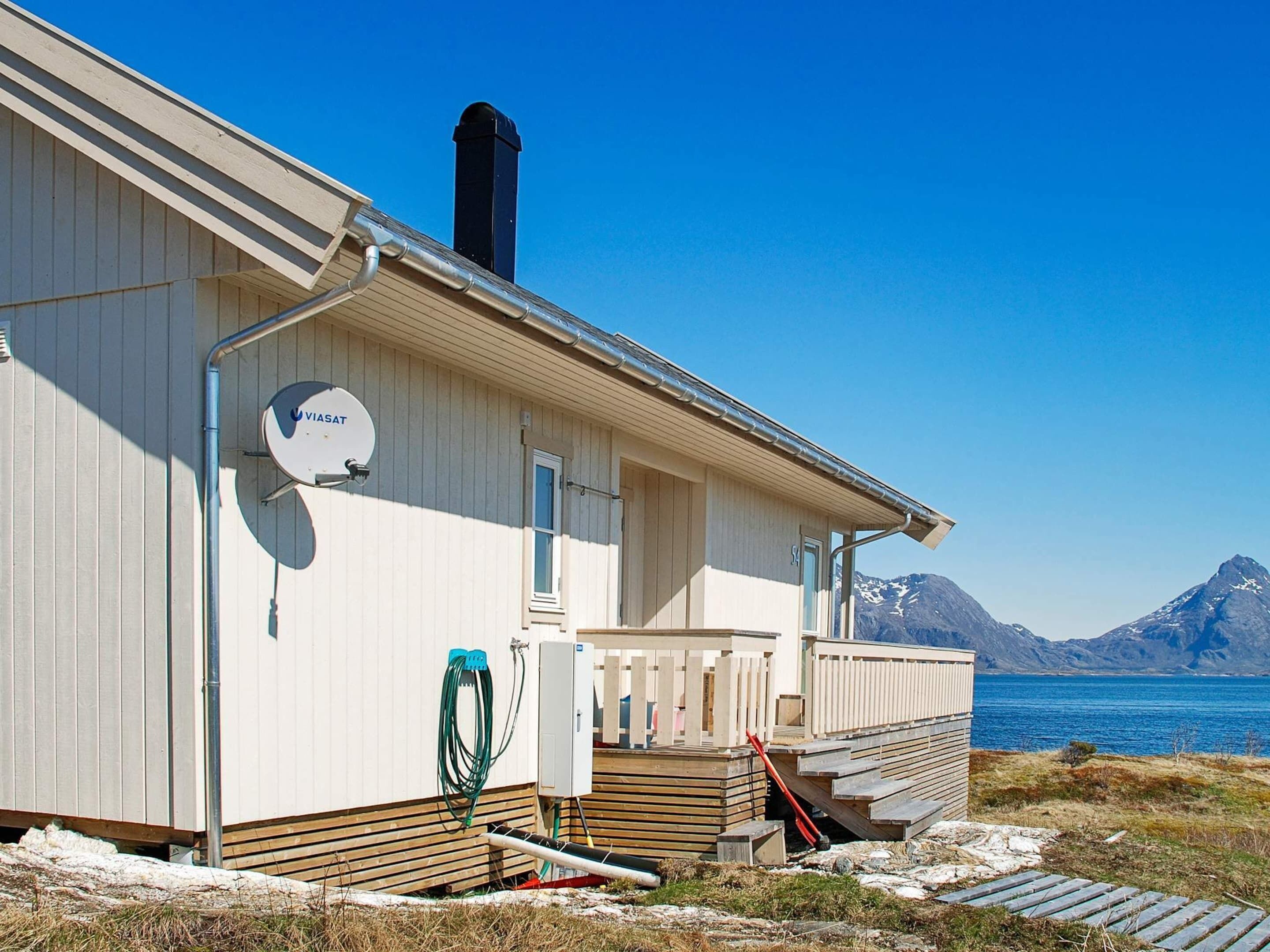 Un bâtiment blanc doté d’une antenne parabolique, d’une cheminée, et offrant une vue sur un lac et des montagnes.