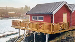 A red cabin with a wooden deck, situated on stilts over water.