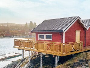 A red cabin with a wooden deck, situated on stilts over water.