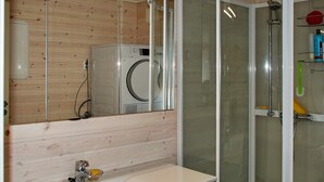 A bathroom with a wooden wall, a washing machine, a glass shower enclosure, and a sink with a mirror.