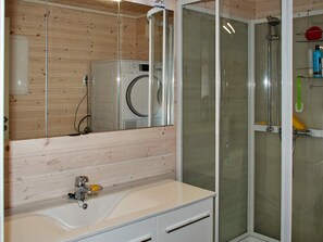 A bathroom with a wooden wall, a washing machine, a glass shower enclosure, and a sink with a mirror.