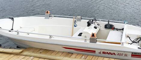 A white motorboat with a cabin, a steering wheel, and a motor on the dock.