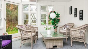 A bright, airy room with wicker furniture, a glass-top table, and a view of greenery outside. - Simplistic Holiday Home in Ringkøbing near Sea (Ringkobing)