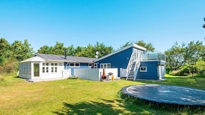 A two-story house with a blue exterior and a white garage. There is a small patio area with a trampoline and a grill. - Simplistic Holiday Home in Ringkøbing near Sea (Ringkobing)