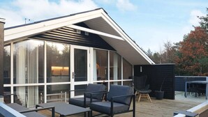 Een modern huis met een schuin dak, grote glasramen en een terras met tuinmeubilair.
