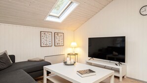 Een moderne woonkamer met een bank, salontafel, televisie en dakraam.