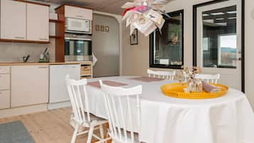 Una cocina moderna con armarios blancos, horno empotrado y un comedor con mesa y sillas blancas.