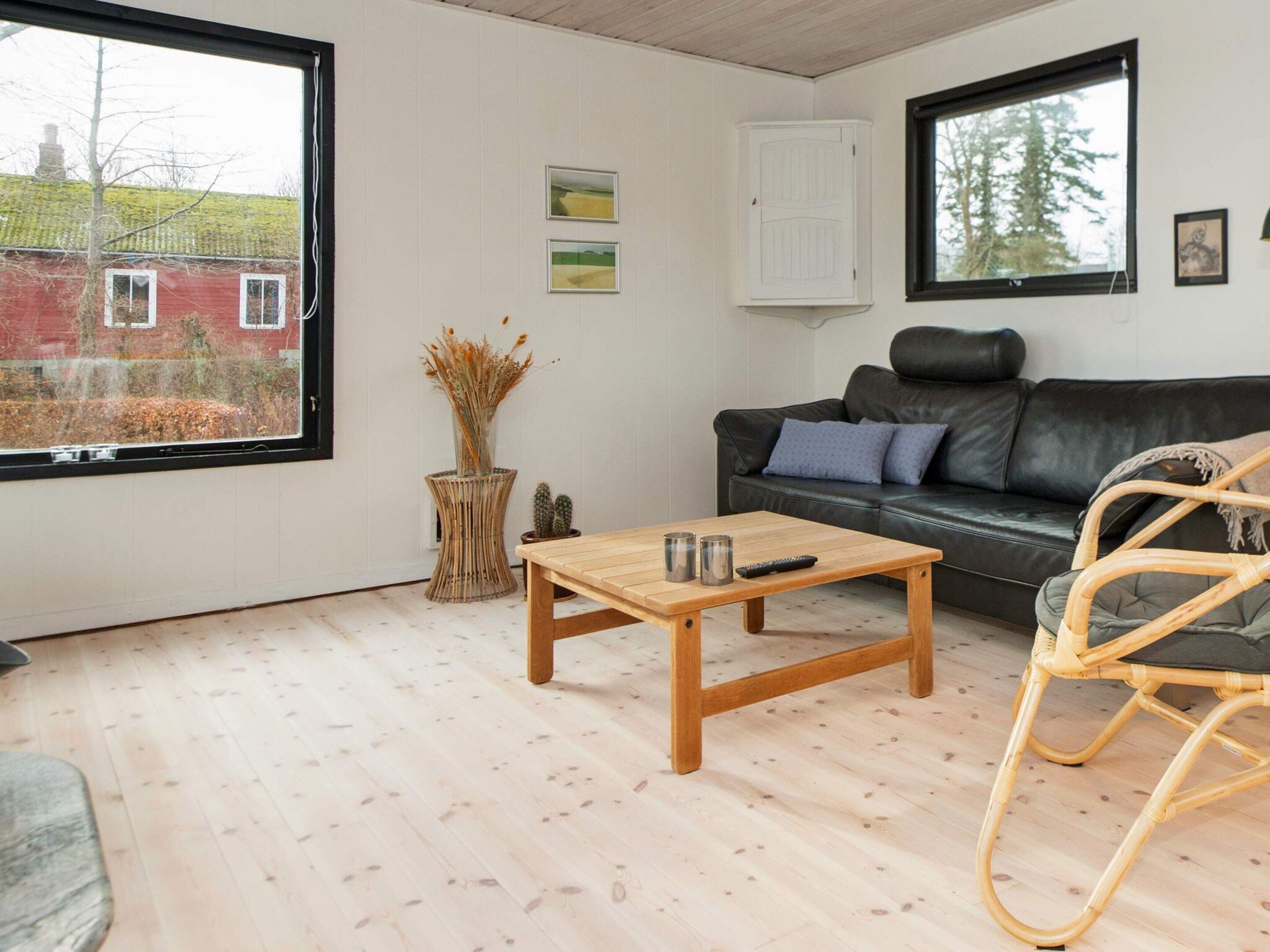 Una sala de estar con un sofá de cuero negro, una mesa de centro de madera, una silla de mimbre y vista a un edificio rojo a través de un ventanal grande.