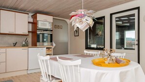 A modern kitchen with white cabinetry, a dining table with white chairs, and a yellow tray with flowers. - 5 Person Holiday Home in Juelsminde-by Traum (Horsens)