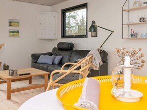 Un salon avec un canapé en cuir noir, une table basse en bois, un fauteuil en osier et un plateau jaune sur lequel est posée une bougie.