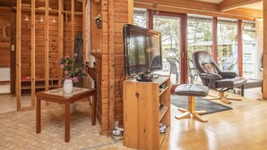 A cozy cabin interior with a wooden interior, a TV on a wooden stand, a dining table with a vase of flowers, and a comfortable seating area with chairs. - Fantastic Holiday Home with Sauna near Roslev (Roslev)