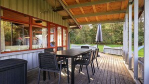 A covered outdoor patio with a wooden table and chairs, a window with a view of the garden, and a white picket fence. - Fantastic Holiday Home with Sauna near Roslev (Roslev)