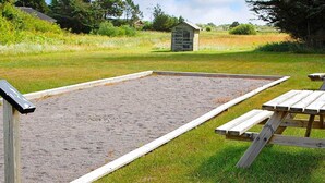 A sandbox area with a wooden frame, a small shed, and a picnic table in a grassy field. - Spacious Retreat by Dunes - By Traum Ferienwohnungen (Hirtshals)
