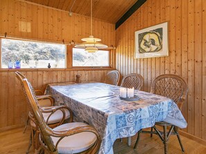 Une pièce aux murs lambrés, avec une table à manger, des chaises en osier et une œuvre d’art encadrée accrochée au mur.