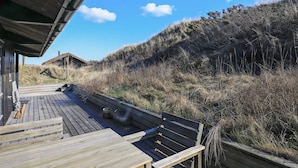 A wooden deck with benches, overlooking a grassy hill and a building in the background. - 6 Person Holiday Home in Skagen (Skagen)