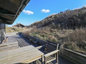 Une terrasse en bois, dotée de bancs, qui offre une vue sur une colline verdoyante et un bâtiment situé au loin.