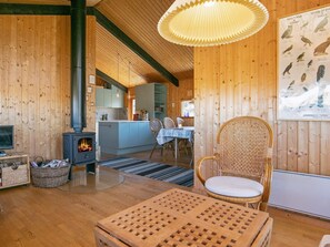 Un intérieur chaleureux, avec des murs en bois, une cheminée, un coin repas et une affiche représentant des oiseaux.