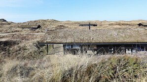 A remote, rustic building with a flat roof, surrounded by dry grass and hills. - 6 Person Holiday Home in Skagen (Skagen)