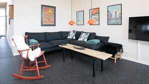 Un salon moderne avec un canapé gris foncé, une table basse en bois, un fauteuil à bascule et un téléviseur fixé au mur.