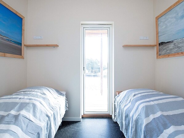 Una habitación con dos camas, una puerta que da al exterior y un pequeño estante sobre cada cama.