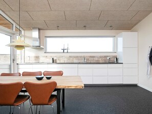 Una cocina moderna con armarios blancos, un ventanal grande y una zona de comedor con mesa de madera y sillas marrones.