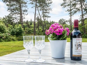 A table with two clear glass wine glasses, a white pot with pink flowers, and a bottle of Bordeaux wine. - 5 Person Holiday Home in Ringkobing-by Traum (Ringkobing)