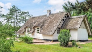 Ein traditionelles Haus mit einem Strohdach und Schornstein, umgeben von Grünflächen und Bäumen.