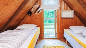 Ein gemütliches Schlafzimmer im Dachgeschoss mit zwei Betten, einem kleinen Fenster mit Moskitonetz und Blick auf Grün.