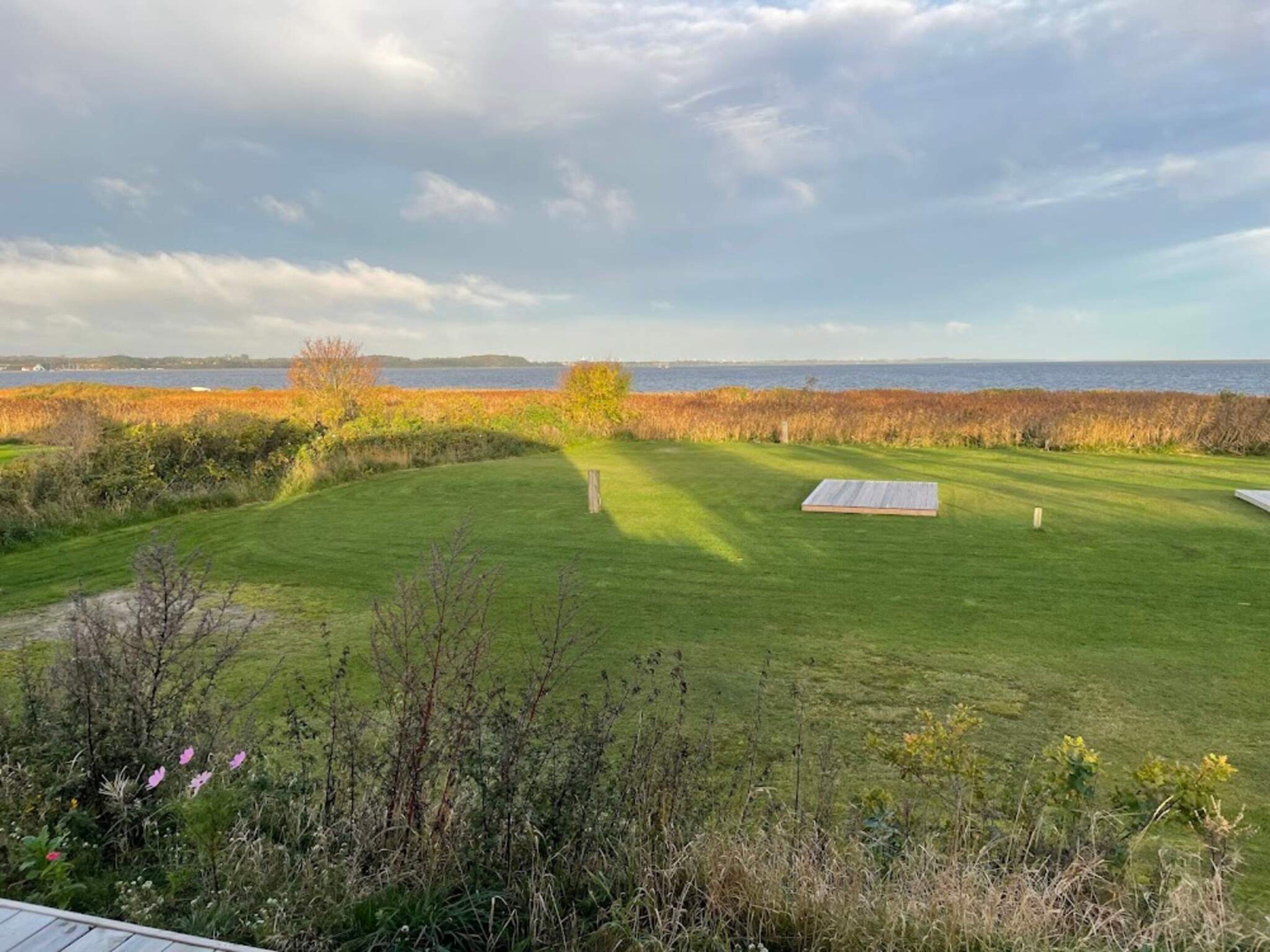 A well-maintained lawn with a wooden deck and a view of the sea.