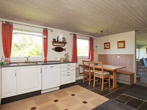 Una cocina con armarios blancos, una mesa de madera y sillas. Hay una decoración de pescado en la pared y una ventana con cortinas rojas.
