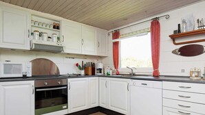 Una cocina con armarios blancos, microondas, horno y lavavajillas.